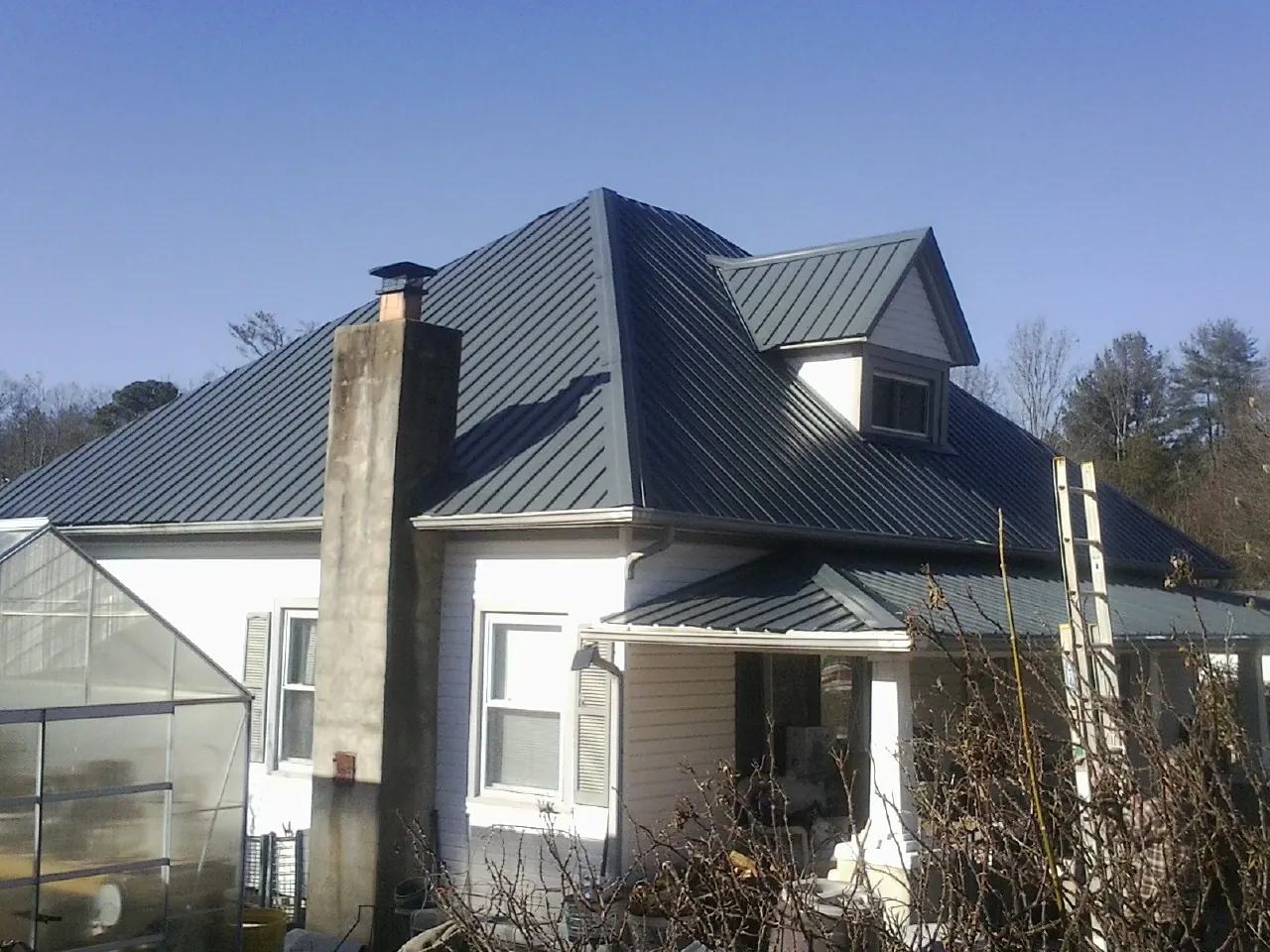 Dark blue standing seam metal roof on a white farmhouse with dormer — Slate & Tile Roof Repair by Roofing Brothers in Carlstadt