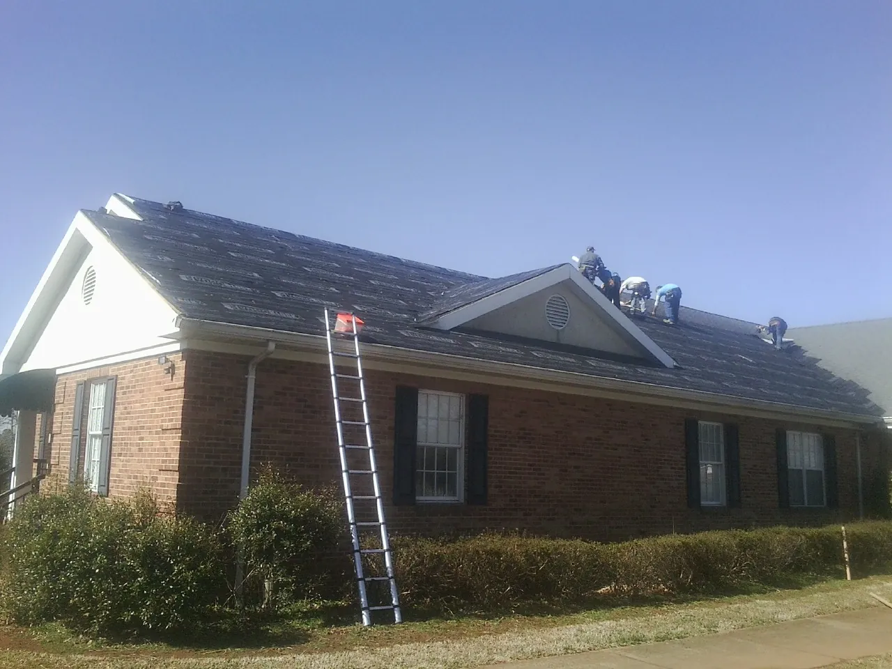 Crew tearing shingles off a brick ranch roof with a ladder set — Metal Roof Repair work by our crew in Carlstadt
