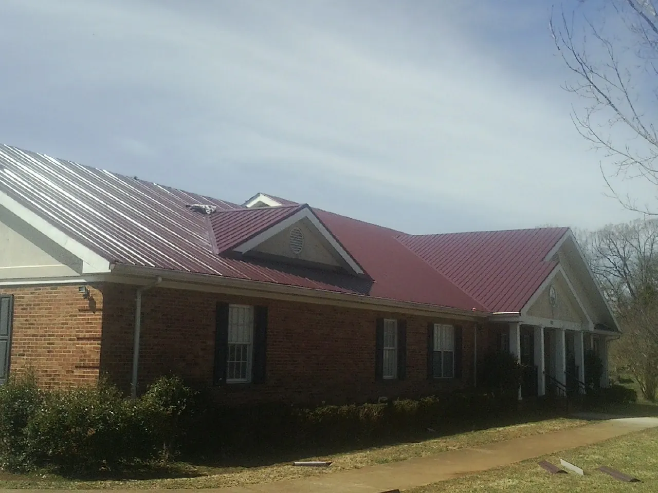 Red metal roof with gabled entries on a long brick building, from a Hail Damage Roof Repair job in Carlstadt