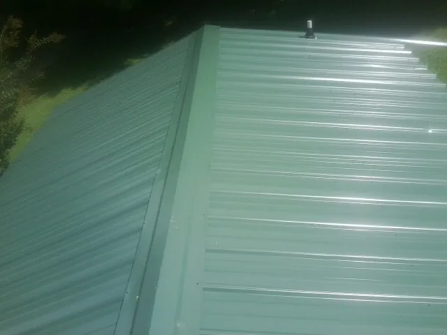 New green metal panels meeting at the ridge of a roof — Flat Roof Repair work by our crew in Carlstadt