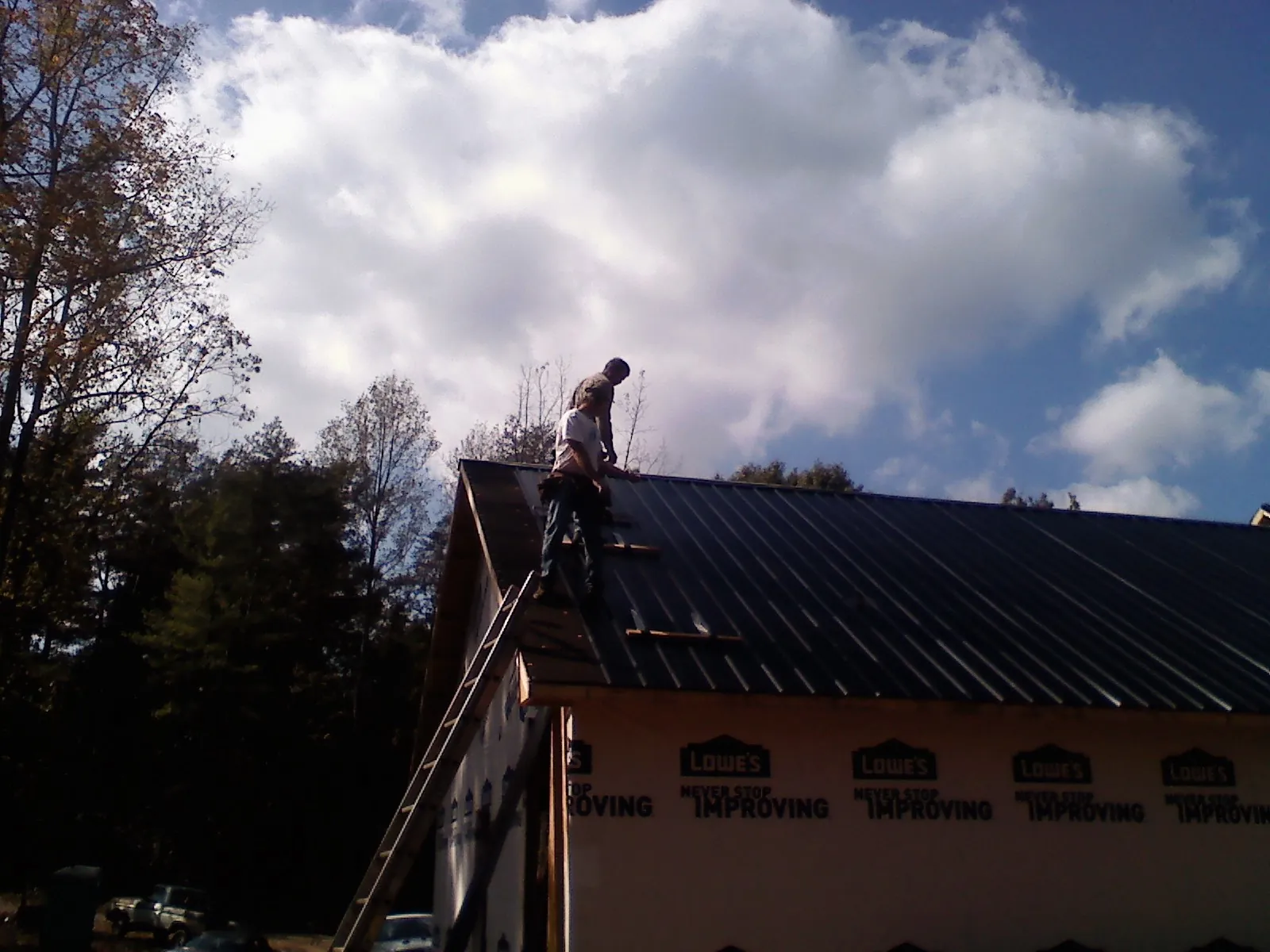 Roofer fastening dark metal panels high against a cloudy sky, from a Roof Inspection job in Carlstadt