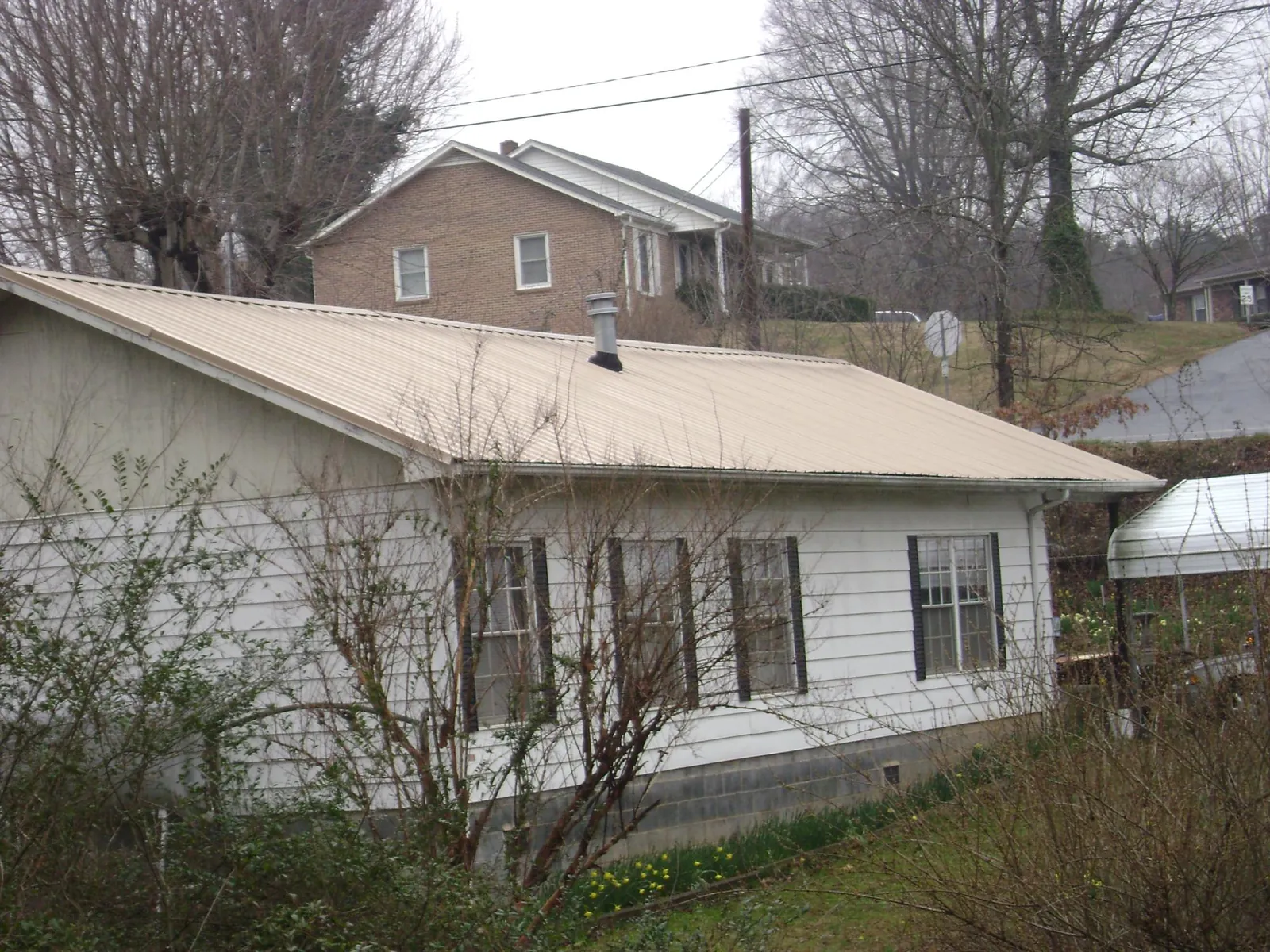 Tan metal roof on a white sided house set into a hillside — Commercial Roofing by Roofing Brothers in Carlstadt